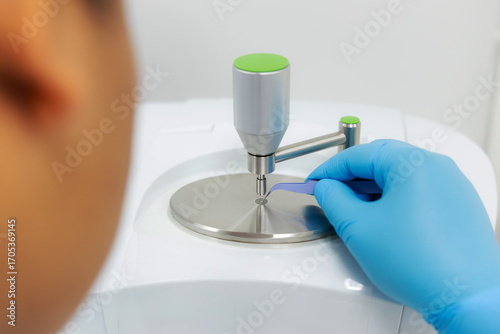Wallpaper Mural A laboratory technician carefully places a sample to the analysis plate of an FT-IR (Fourier Transform Infrared) spectrometer using tweezers prepared for precise material laboratory technology. Torontodigital.ca