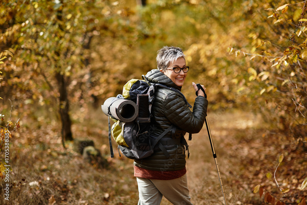 Naklejka premium Enjoying the tranquility of nature, a senior woman hikes through a vibrant autumn forest trail