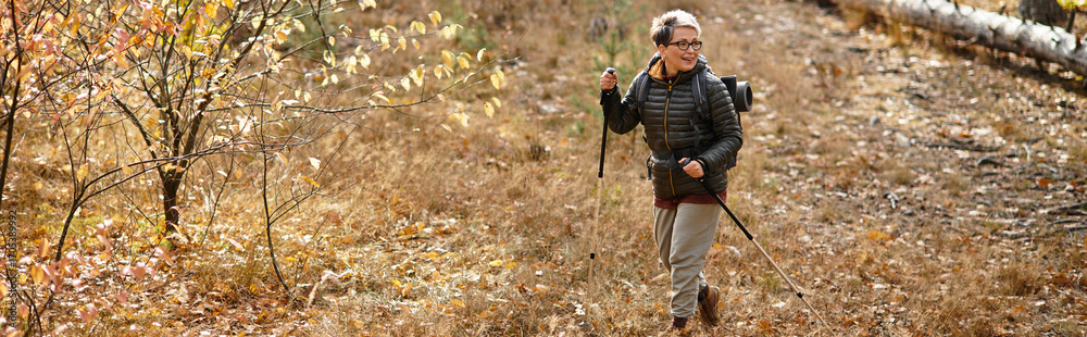 Fototapeta premium Joyful hike through golden autumn forest by a senior woman enjoying nature