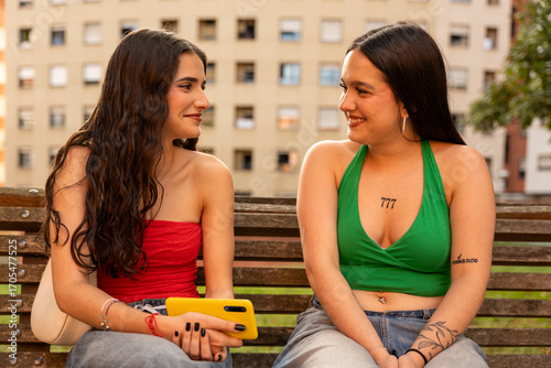 Two young women talking and smiling on a bench in the city
