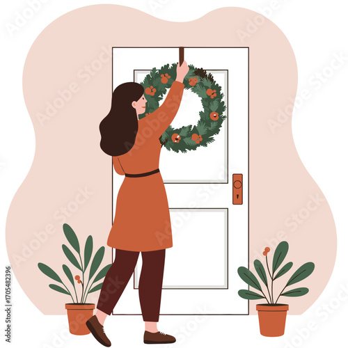 Woman hanging a Christmas wreath on door with plants nearby  