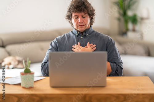 Man Meditating with Hands on Chest in Front of Laptop