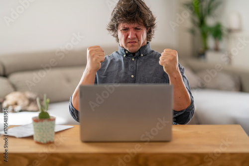 Man Celebrating with Clenched Fists in Front of Laptop at Home