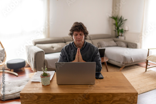 40-year-old man praying in front of laptop for good news while working in home office