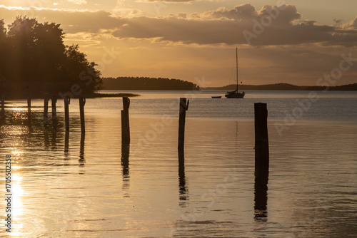 Amazing golden sunset behind the clouds during spring, over the world biggest archipelago near the city Turku seen from the village of Naantali, with calm water and a row of poles for boats to dock 