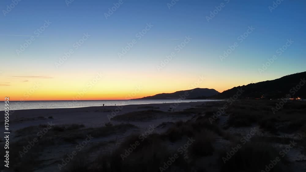 Drone view of vibrant sunset over the ocean, with a wide dark beach in the foreground Drone view of vibrant sunset over the ocean, with a wide dark beach in the foreground