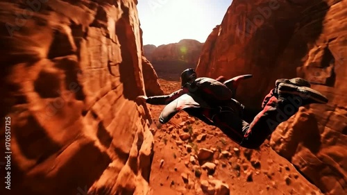 A wingsuit flyer skillfully navigates through a narrow sunlit red rock canyon performing an exhilarating and dangerous feat of proximity flying.
