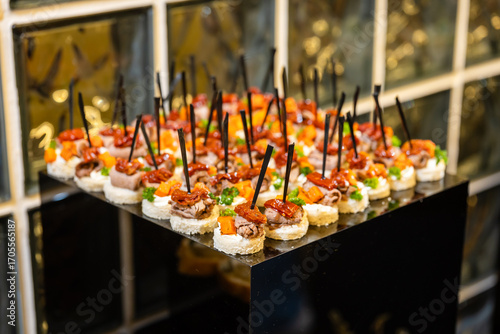 Canapes with meat and vegetables on black stand elegant appetizers at event.