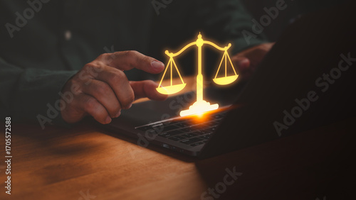 Photography Businessman using laptop with glowing golden justice scales icon, symbolizing law, fairness, legal advice, and online court services in modern digital technology and business ethics