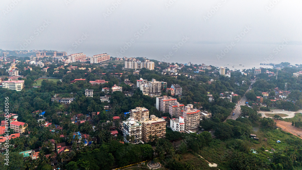 Obraz premium Aerial shot of Caranzalem and Dona Paula in Goa, showcasing houses, buildings, and lush greenery with the sea and winter sky in the background.