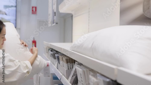 Asian woman examining soft white bed pillow in home goods store, carefully selecting bedding accessory for comfort and quality, retail shopping lifestyle and bedroom sleep product choice