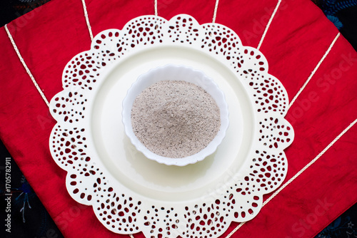 Kuttu ka Aata or Buckwheat flour in a white bowl with white and red background. gluten-free, nutrient-rich flour consumed during Hindu fasting days like Navratri and Ekadashi