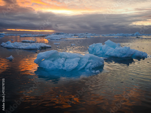Floating icebergs in calm Arctic water reflecting vibrant sunset sky and dramatic clouds