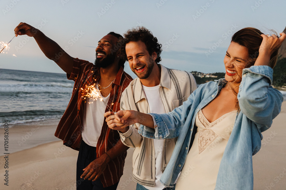 Fototapeta premium Friends enjoying sparklers and celebrating together on a beach at sunset