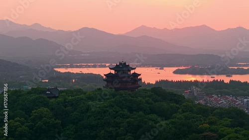 Aerial view of Chenghuang pagoda at sunset over Xihu lake in Hangzhou featuring mountains and lush green trees