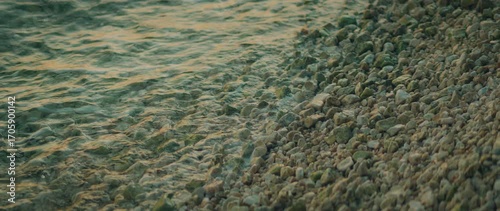 Sea waves gently rolling over smooth stones on a quiet shoreline at sunset close-up