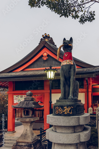 Traditional fox statue at Fushimi Inari Taisha Kyoto Japan standing near stone lantern and gate illuminated by gentle early morning sunlight