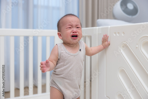 Upset baby crying and standing in playpen