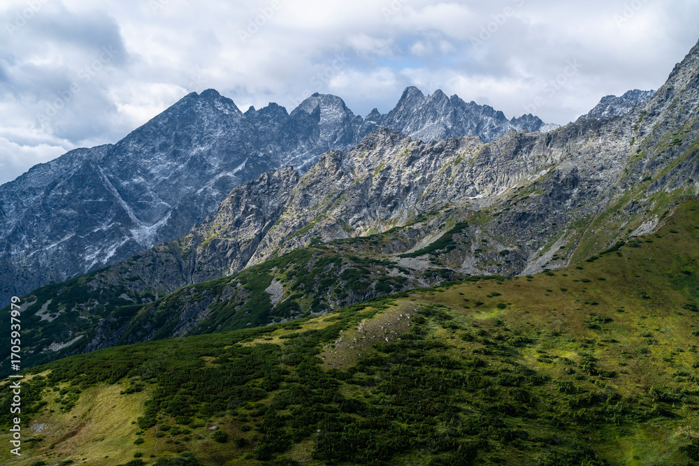Fototapeta premium Panorama of the lightly snow-covered peaks and slopes of the higher mountains in summer.
