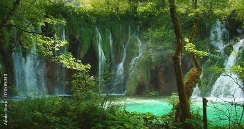 Lush green forest and stunning cascading waterfalls surround emerald lake