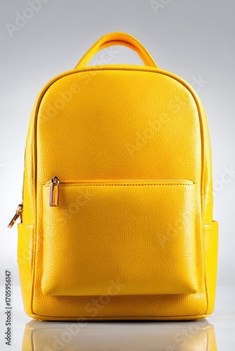 Bright yellow rectangular backpack, with a front pocket & handle on top, standing on a reflective white surface against a soft gray backdrop