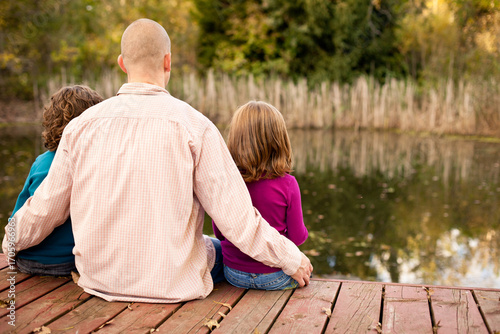 Dad and Daughters Sitting Together on Deck at Water's Edge