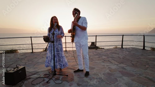 Couple musicians performing on stone terrace with cables and equipment at sunset