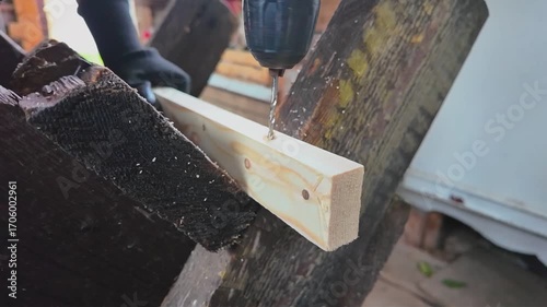 A male carpenter drills a hole in a wooden block with an electric drill. Slow motion
