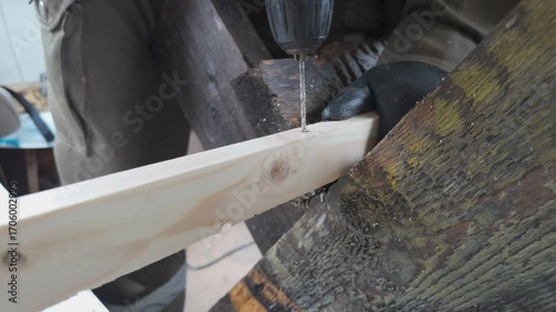 A male carpenter drills a hole in a wooden block with an electric drill. Slow motion