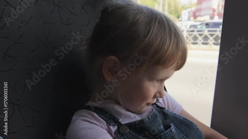 A child, a five-year-old girl rides a bus and looks out the window