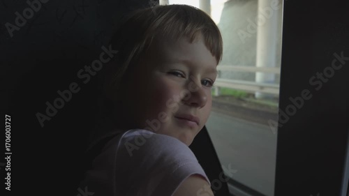 A child, a five-year-old girl rides a bus and looks out the window