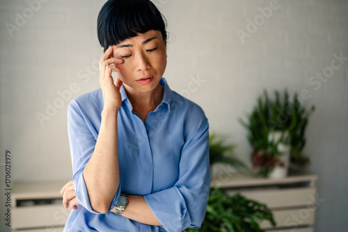 Stressed Asian woman touching her temple, showing headache, fatigue, anxiety, or emotional struggle in daily life