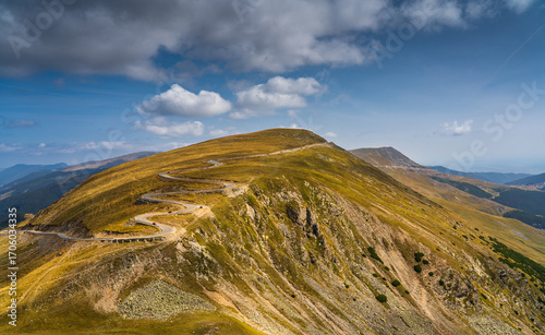 A solo traveler experiences a breathtaking autumn day in the wild Carpathian Mountains, near Lake Galcescu, in the Parang Mountains of Romania, where vibrant fall colors meet rugged peaks