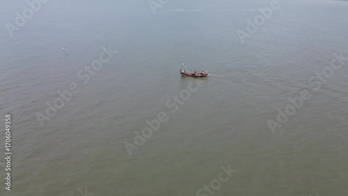 Aerial view of a wooden boat sailing on a murky sea. Drone footage follows the boat.