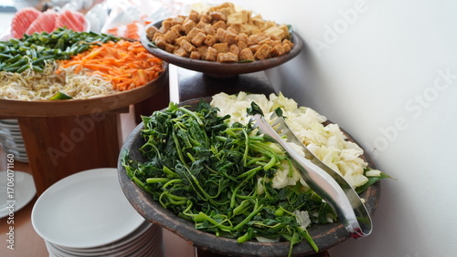 buffet station with fresh vegetables and tofu in wooden bowls, leafy greens, carrots, sprouts, onions, and cubed tofu gently shifting under ambient light in clean self-serve setup