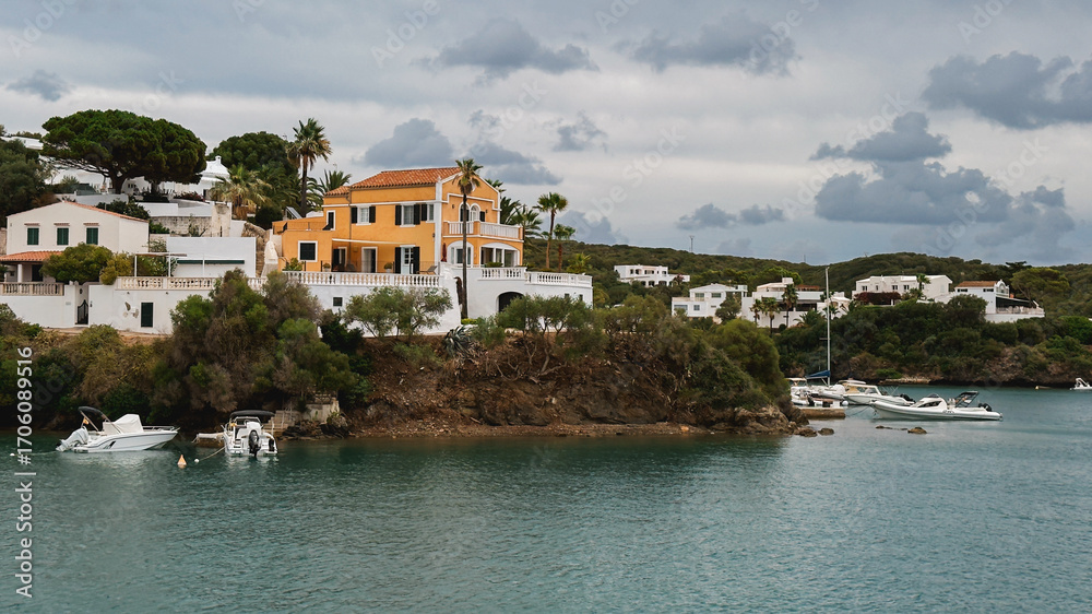 Fototapeta premium Coastal villa with orange walls and white details overlooking a calm bay. Menorca, Mahon