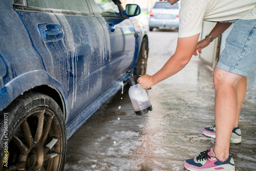 A person is spraying foam onto a car in a car wash facility, taking care to clean the vehicle thoroughly in a bright environment
