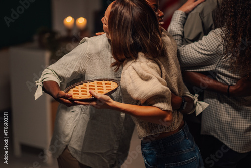 Friends bringing pie and hugging at thanksgiving dinner