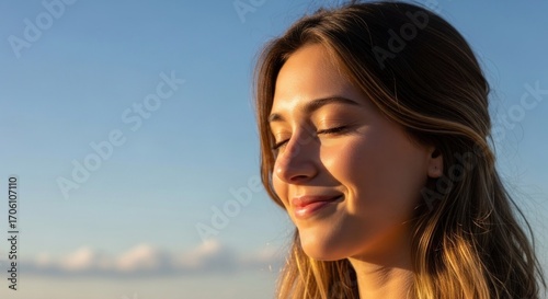 A serene young woman gazes thoughtfully into the distance against a soft, light-blue sky.