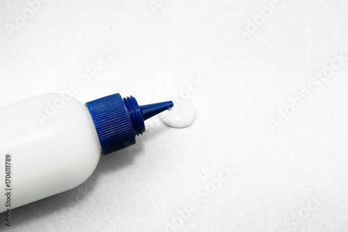 Close up of white glue bottle with blue cap dispensing adhesive on textured surface