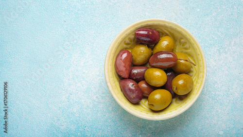Green and black olives, glistening with oil in a ceramic bowl on a vibrant light blue backdrop top view, copy space