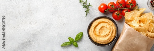Delicious hummus served with crispy chips, fresh cherry tomatoes, and aromatic herbs, perfect for healthy snacking or entertaining guests at a gathering.