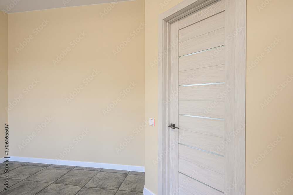 Fototapeta premium Interior shot of a modern room featuring a sleek, light wood door with glass accents, set against pale yellow walls and a tiled floor