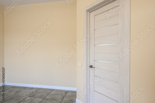 Interior shot of a modern room featuring a sleek, light wood door with glass accents, set against pale yellow walls and a tiled floor