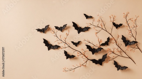 Black paper bats are artistically arranged on a soft beige wall alongside bare branches adorned with delicate autumn leaves, creating a seasonal decoration that adds charm.