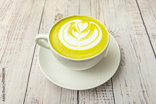 A clear cup with a modern, frothy matcha latte, viewed from above against a light brown background, highlighting its texture and green hue
