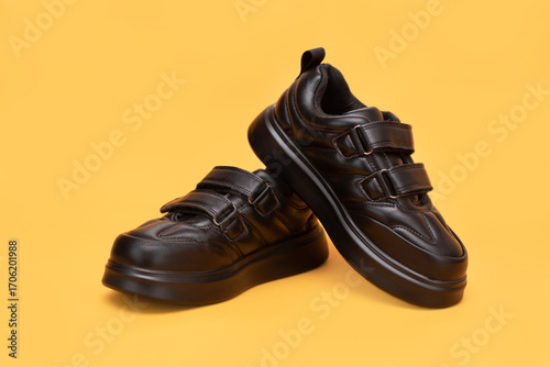 Close-up of a pair of black velcro sneakers elegantly positioned on a vibrant yellow backdrop, emphasizing their stylish design. Comfortable autumn and spring shoes for young boys, waterproof