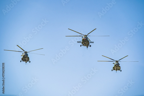 Military helicopters fly in formation across a clear blue sky during a training exercise near a coastal region