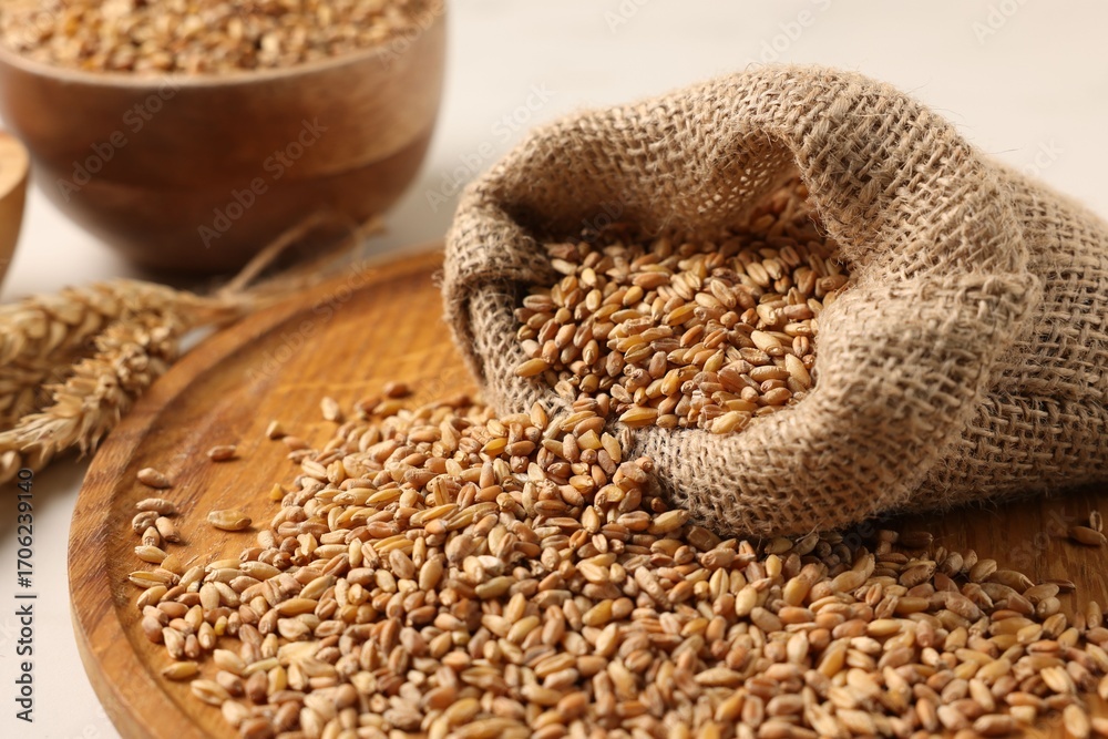 Obraz premium Wheat grains, spikes and burlap sack on white table, closeup