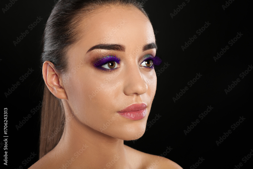 Fototapeta premium Young woman with beautiful makeup and purple eyelashes against black background, closeup